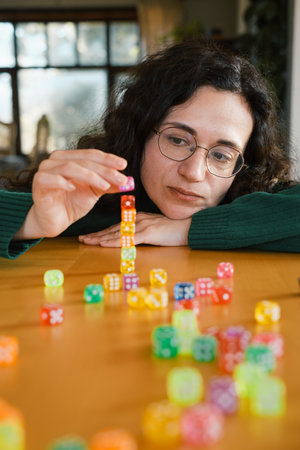 Woman focused on building tower from dice. Balance and patience developed during fun leisure activity. Adult hobbyの写真素材