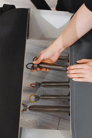 Selecting elastic springs on the reformer for pilates. Closeup of hand adjusting pilates equipments in fitness studio focusing on strength, flexibility and body control Preparation for pilates sessionの写真素材
