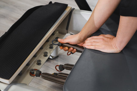 Selecting elastic springs on the reformer for pilates. Closeup of hand adjusting pilates equipments in fitness studio focusing on strength, flexibility and body control Preparation for pilates sessionの写真素材