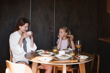 Mother and daughter having meal together in a stylish, contemporary home. Family eating delicious breakfast on the kitchenの写真素材