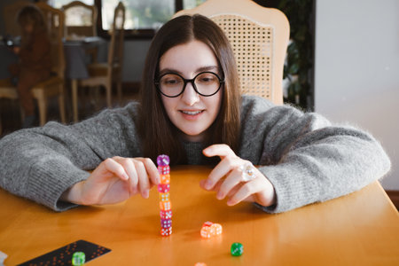 Woman building colorful stack of dice during tabletop game in bright living room. Happy smiley female enjoy playing game at homeの写真素材