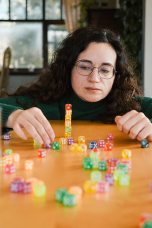 Woman focused on building tower from dice. Balance and patience developed during fun leisure activity. Adult hobbyの写真素材