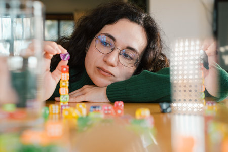 Woman focused on building tower from dice. Balance and patience developed during fun leisure activity. Adult hobbyの写真素材
