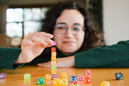 Woman player at her 40s stacking colorful dice during table game night. Female enjoys activity and fun free time entertainmentの写真素材