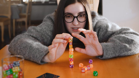 Woman building colorful stack of dice during tabletop game in bright living room. Happy smiley female enjoy playing game at homeの写真素材