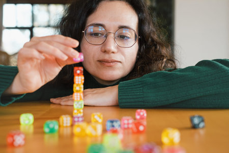 Woman focused on building tower from dice. Balance and patience developed during fun leisure...