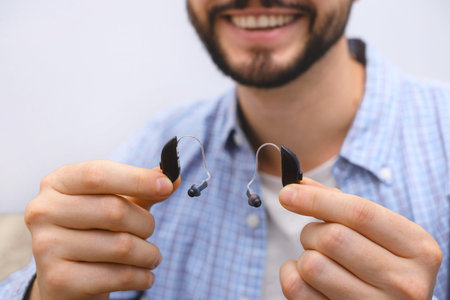 Closeup Smiling man in his 30s shows modern hearing aids in hands