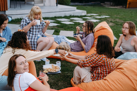 Big group of friends lounge on colorful bean bags outdoors with food