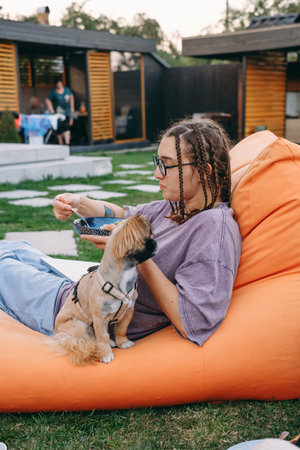 Young woman with braids eating on the lawn with small dog