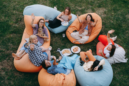 Group of friends relaxing on colorful bean bags outdoors, sharing meal