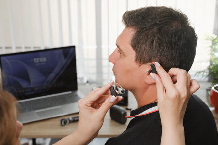 Audiologist fitting a behind-the-ear hearing aid for a manの写真素材