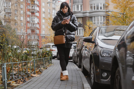 Confident urban woman strolls past fully parked cars, chatting on mobile phoneの写真素材