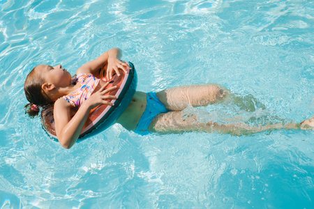 Relaxed girl floating on watermelon inflatable ring in blue swimming pool