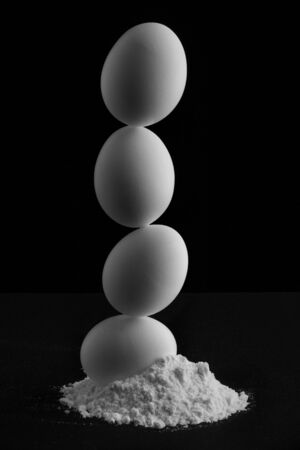 Balanced and Staked Eggs in White Flower on Black Backdropの写真素材