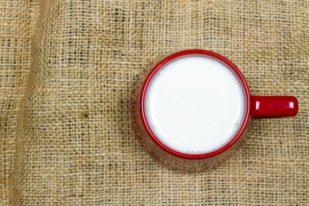 Top view of milk in red ceramic cup or mug on sackcloth background with copy space. Milk is a high-protein beverage, suitable for everyone.の写真素材