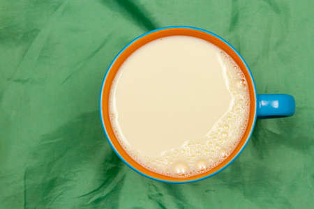 Top view of milk in blue and orange ceramic cup or mug on green cloth background with copy space. Milk is a high-protein beverage, suitable for everyone.の写真素材