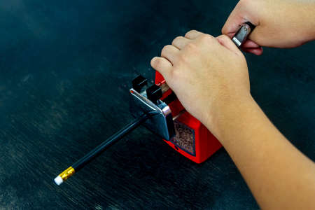 Girl hands sharpening black pencil with red sharpener on black background.の写真素材