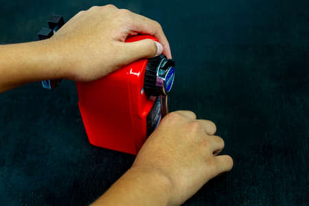 Girl hands sharpening black pencil with red sharpener on black background.の写真素材