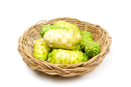 Noni or Morinda Citrifolia fruits in basket isolated on white background. Noni leaves are high...