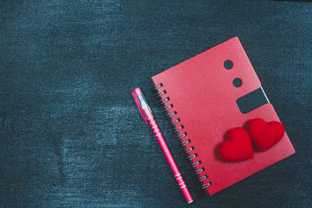 Two red hearts on red notebook and pen on black wooden background, dark tone, valentine's day concept, copy space.の写真素材