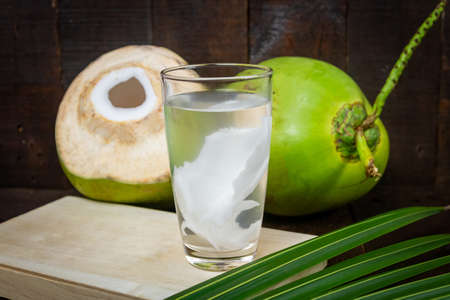 Fresh coconut juice in glass and coconut green leaf on wooden background.の写真素材