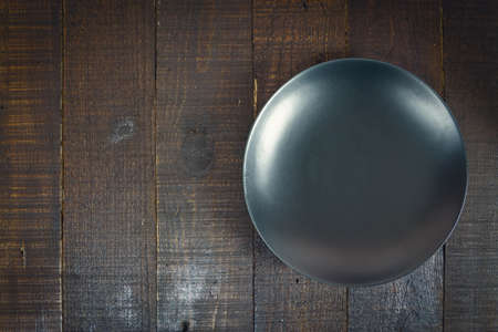 Empty black ceramic plate on wooden background dark tone, copy space.の写真素材