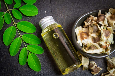 Oil of Moringa in bottle, green leaves and seeds on wooden background. Moringa oleifera tropical herb product concept.の写真素材