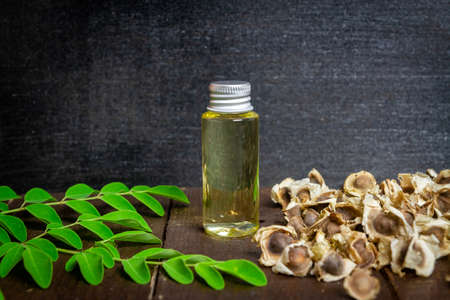 Oil of Moringa in bottle, green leaves and seeds on wooden background. Moringa oleifera tropical herb product concept.の写真素材