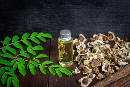 Oil of Moringa in bottle, green leaves, pods and seeds on wooden background. Moringa oleifera tropical herb product concept.の写真素材