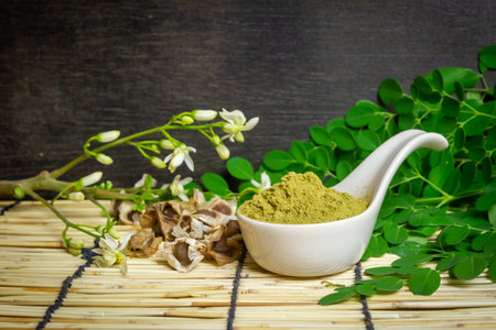 Moringa oleifera powder in white ceramic and green leaves on wooden background. Moringa products concept.の写真素材