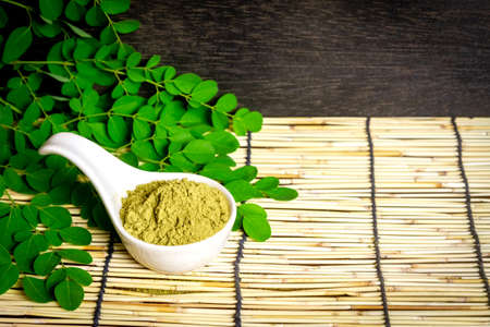 Moringa oleifera powder in white ceramic and green leaves on wooden background. Moringa products concept.の写真素材