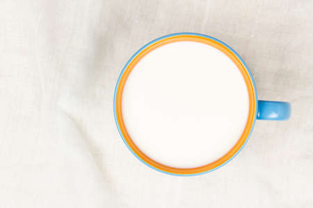 Top view of milk in blue and orange ceramic cup on white cloth background with copy space.の写真素材