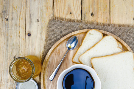 Top view of sliced bread, orange jam and black coffee on wooden plate, black background dark tone.の写真素材