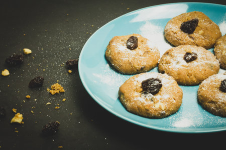Fresh Oatmeal raisin cookies on blue sky ceramic plate and black background, dark food concept.の写真素材