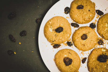 Fresh Oatmeal raisin cookies on pink ceramic plate and black background, dark food concept. Copy space.の写真素材