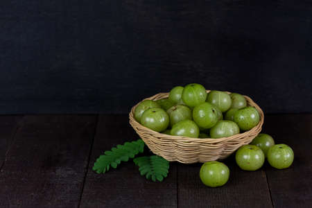 Pile of Indian gooseberry fruits or Amla (phyllanthus emblica) on wicker basket on wooden background, dark tone.の写真素材
