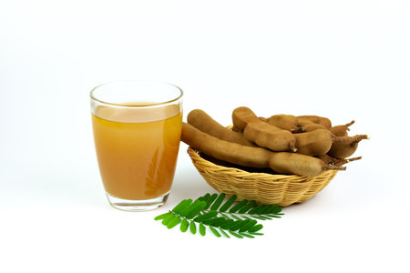 Tamarind juice in glass and tamarind fresh tropical fruit in wicker basket with leaf isolated on white background.の写真素材