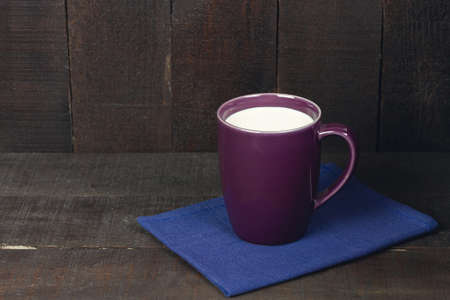 Purple cup of milk on blue cloth on brown wooden background. Dark tone.の写真素材