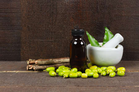 Neem oil in bottle and Neem leaf in mortar and pestle white ceramic with stick and fruit on wooden background.の写真素材