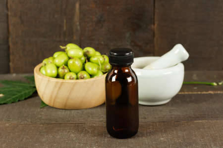 Neem oil in bottle with neem fruit in wooden bowl and mortar and pestle on wooden background.の写真素材