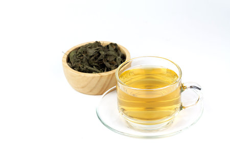 Tulsi or holy basil tea in transparent cup with dried tulsi leaf in wooden bowl isolated on white...