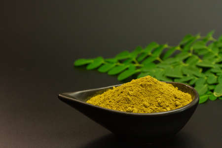 Moringa powder in black bowl ceramic and fresh moringa green leaf on black background.の写真素材
