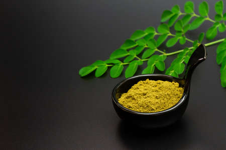 Moringa powder in black bowl ceramic and fresh moringa green leaf on black background.の写真素材