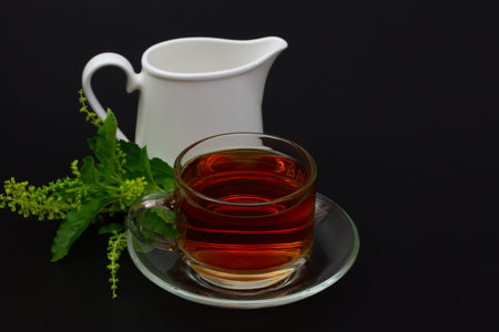 Holy Basil or tulsi tea in transparent glass cup and holy basil leaf on black background. Popular...