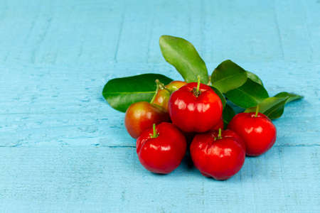 Pile of Acerola Cherry or Barbados Cherry with leaf on blue wooden background.の写真素材