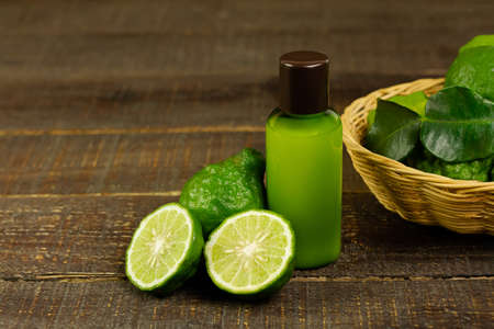 Shampoo made of bergamot in green plastic bottle and fresh bergamot fruit and sliced with wicker basket on brown wooden background. Natural products used to care for hair and scalp concept.の写真素材