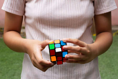 SAMUT-SAKHON, THAILAND - APRIL 04, 2021 : Hands of a young girl trying to solve the Rubik's Cube puzzle on the grass field.のeditorial素材