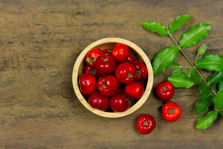 Acerola Cherry or Barbados Cherry with leaf in wooden bowl on wooden background, Top view.の写真素材
