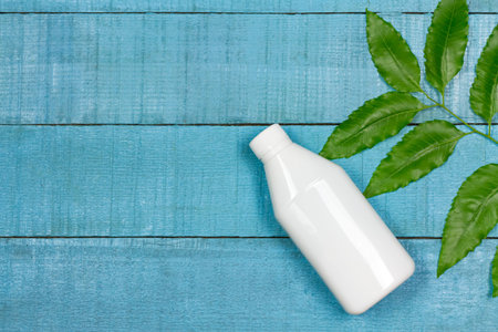 Neem oil in white plastic bottle with neem leaf on blue wooden table, top view. Pure neem oil ultra...