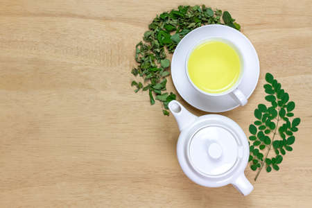 Moringa Tea in white cup and fresh green leaf with teapot on wooden background, top view. Moringa oleifera tropical herb healthy lifestyle concept.の写真素材